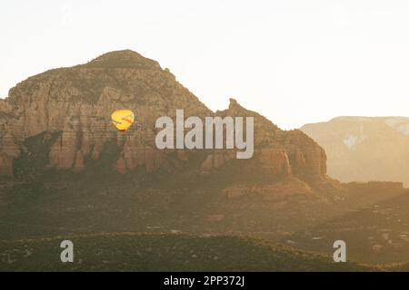 Horizontal image of wide shot of yellow hot air balloon releasing flames to gain altitude in early morning flight. Stock Photo