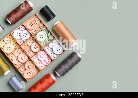 Composition with box of different buttons and thread spools on grey background Stock Photo