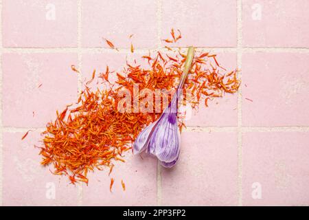 Heap of dried saffron threads and crocus flower on pink tiled table Stock Photo