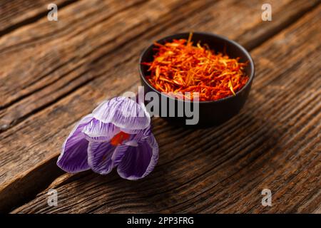 Bowl of dried saffron threads with crocus flower on wooden table Stock Photo