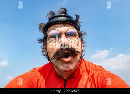 An emotional cyclist drives on a bicycle in a retro helmet under a blue sky Stock Photo