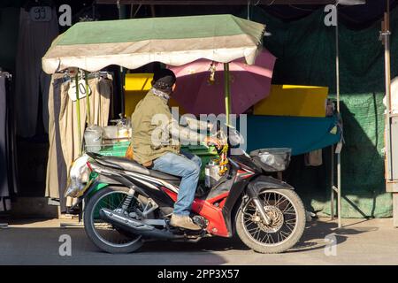 An ice cream vendor rides a three-wheeled motorcycle on a street with stands, Bangkok, Thailand Stock Photo