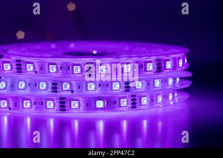 Roll of LED strip with bright neon purple lamps placed on table in dark room Stock Photo