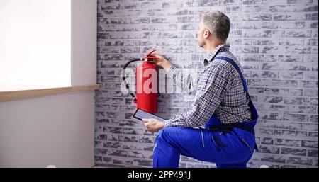 Worker Installing Fire Extinguisher. Inspection Service. Checking Security Label Stock Photo
