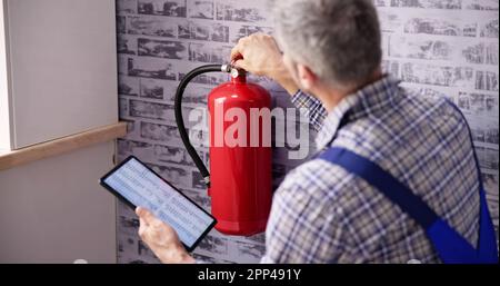 Worker Installing Fire Extinguisher. Inspection Service. Checking Security Label Stock Photo