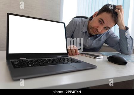 Young tired business man rubbing his head sitting at table in front of laptop in his office Stock Photo