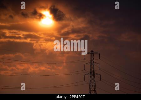 Dramatic sky and sunset over the Worcestershire countryside with electric power pylons silhouetted against the orange spring sky, England. Stock Photo