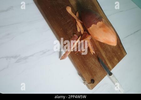 Sweet potato being prepared on wood cutting board on marble kitchen top Stock Photo