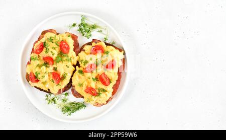 Scrambled eggs with microgreen, bacon and tomatoes on bread over stone background with copy space. Top view, flat lay Stock Photo