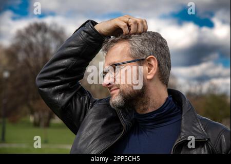 A 50 years old man in the black leather jacket scratching his head while thinking about a problem Stock Photo