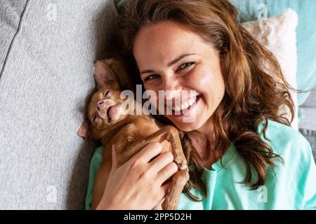Top view portrait of funny sleeping small red color dog and happy woman. Stock Photo