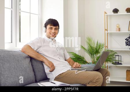 Cheerful male student freelancer at home watching online training or webinar on laptop. Stock Photo