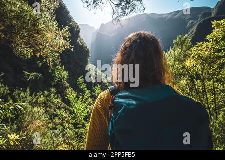Description: Tourist woman enjoying view from water channel hiking trail at steep cliff through Madeira's rainforest. Levada of Caldeirão Verde, Madei Stock Photo