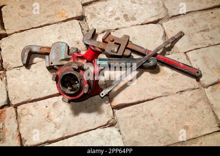 old rustic used Pipe wrench, hexa blade, manual threading machine on brick background. Stock Photo