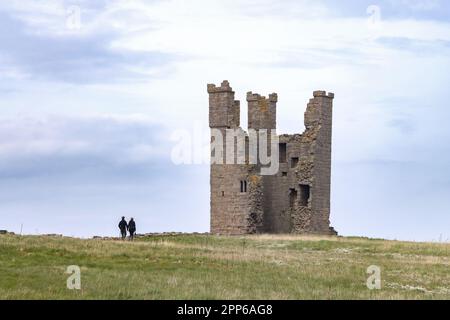A couple walking at Dunstanburgh Castle, a 14th Century ruined medieval castle on the coast, Northumberland UK Stock Photo
