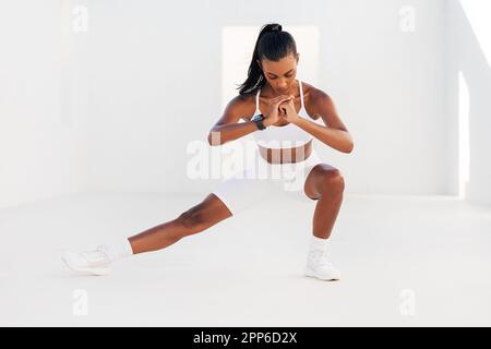 Strong female athlete in white fitness attire stretching body. Young woman warming up before exercises. Stock Photo