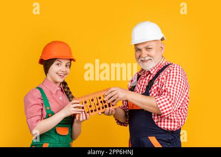 happy teen child and grandfather bricklayer in helmet on yellow ...