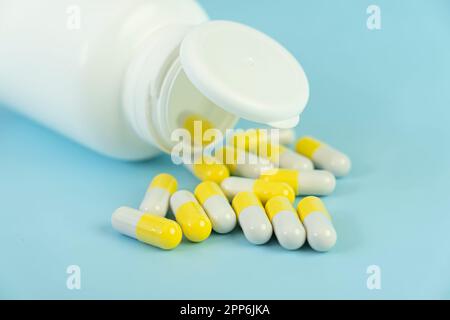 A pile of yellow pills scattered from a white plastic jar on a blue table. the concept of health medicine and pharmacy. Production of medicines. Stock Photo