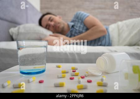 Man sleeping - pills on bed table. a man sleeps on a bed during the day in the foreground is a table with pills and a glass of water. Sleeping pills f Stock Photo