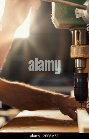Carpenter uses drill press in his workshop. With his left hand, taking calculated risks, he holds and guides the wood, while lowering the lever with h Stock Photo