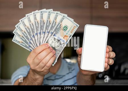 man wears casual clothes blue shirt in hand fan of cash money in dollar banknotes use mobile cell phone. an empty white screen on a smartphone to adve Stock Photo