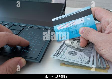 Man holding credit card in hand and entering security code using laptop keyboard. shopping online or transferring money between bank accounts. Stock Photo