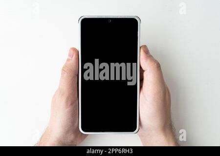 Mockup of male hand holding black frameless cell phone with blank screen at white background. Stock Photo