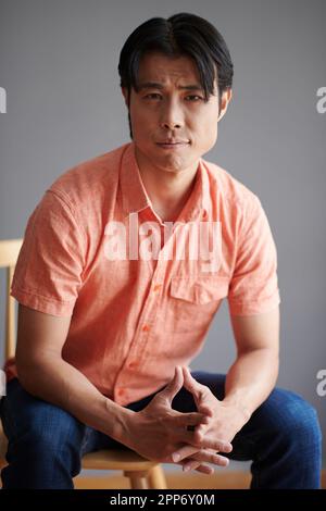 Young man in salmon shirt sitting on chair and looking at camera Stock Photo