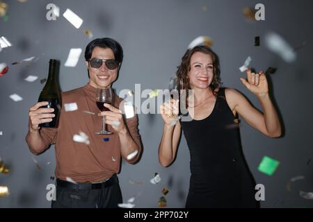 Happy man and woman drinking booze and dancing under falling confetti Stock Photo
