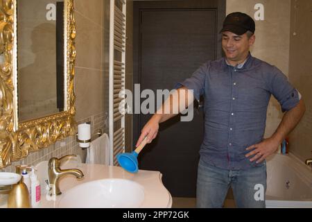 Image of a plumber in a bathroom pointing with a plunger at a clogged sink that needs repairing. DIY work at home. Stock Photo