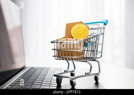 Bitcoins in a toy shopping cart on the laptop. Online shopping concept.  Stock Photo