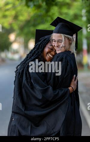 Two Female Graduates Hug Each other after Graduation Ceremony to Celebrate Educational Success and Academic Degree from University. Stock Photo