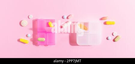Brightly lit plastic organizer with colourful pills, painkillers, vitamins, nutritional dietary supplements isolated on pink background, top view. Stock Photo