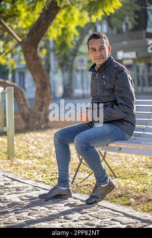 Young latin man sitting on a square bench. Stock Photo