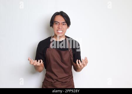 Portrait of annoyed Asian barista man in brown apron making angry hand gesture with fingers. Isolated image on white background Stock Photo