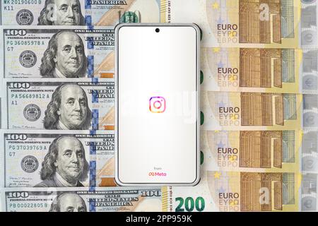 Instagram logo mobile application on screen of smartphone and money background of euro and dollar bills. Close-up, top view. March 30, 2023. Barnaul. Stock Photo