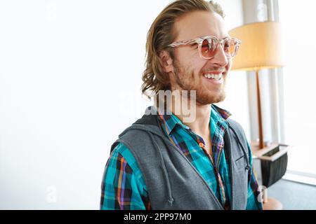 Rocking this style. A handsome young man in a trendy outfit laughing while standing in a home interior and laughing while looking stylish. Stock Photo