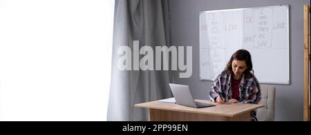 Professional female teacher having online call with students using laptop, writing and taking notes in her notebook. E-learning and online course Stock Photo