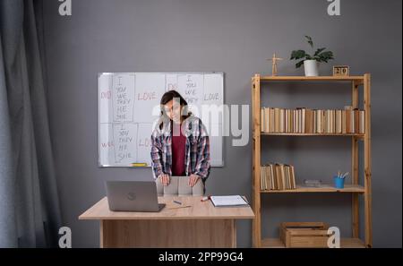 Free time hobby or work remotely. Serious adult woman explaining rules of English and looking at laptop web camera at table in living room Stock Photo