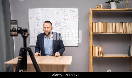 Male English teacher having video conference chat with students and class group, using smartphone. Millennial man talking to webcam, explaining rules Stock Photo