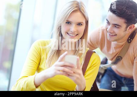 Using her cellphone to reel him in. Young teen couple reading texts on a cellphone. Stock Photo