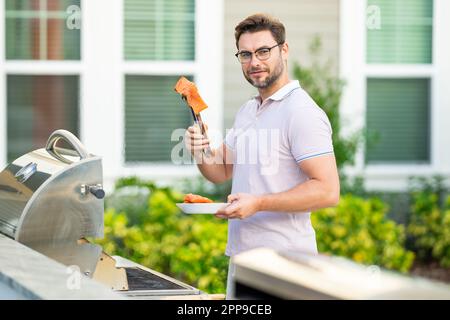 Male chef grilling and barbequing in garden. Barbecue outdoor garden party. Handsome man cook preparing barbecue salmon. Concept of eating and cooking Stock Photo