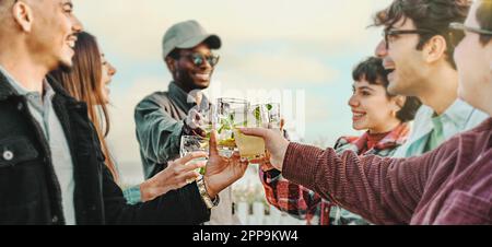 A panoramic shot of a circle of multicultural young friends toasting with mojito glasses, smiling and looking at each other. Focus on the glasses. Stock Photo
