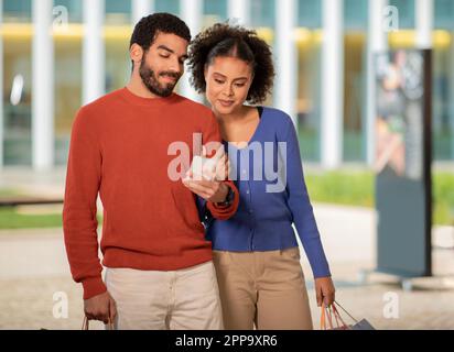 Middle Eastern Buyers Couple Shopping Using Cellphone Standing Outside Stock Photo