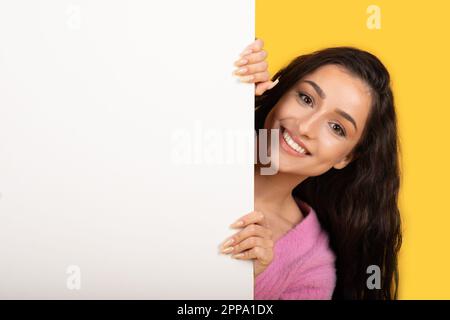 Smiling young arab lady peeks out from behind big banner with empty space for ad, text and offer Stock Photo