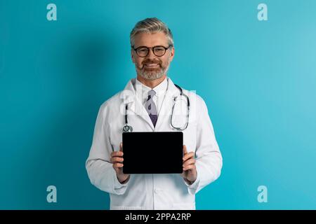 Cheerful middle aged doctor showing digital tablet with blank screen Stock Photo