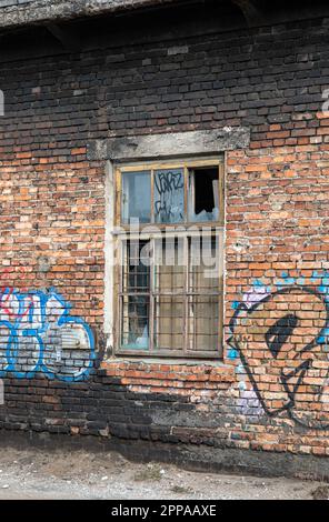 Broken window on old graffiti covered derelict red brick building Stock Photo