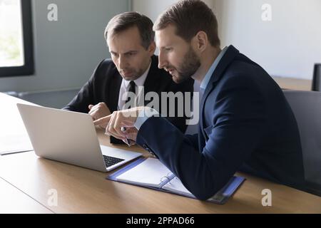 Two focused businessmen staring at laptop display at table Stock Photo