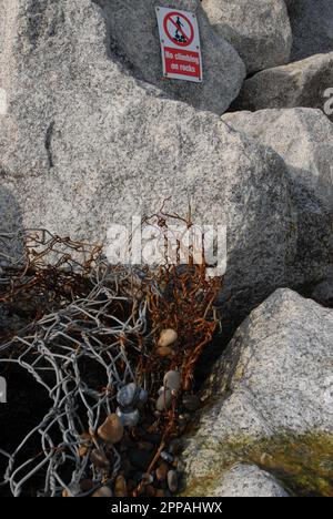 Broken pieces of wire gabion flood defence on 35-metre rock revetment, with sign saying no climbing on the rocks. Thorpeness Beach. 15th February 2023 Stock Photo