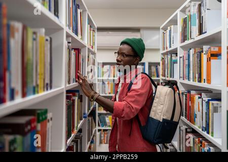 Thoughtful African American student man in glasses choosing book in college library or bookstore Stock Photo
